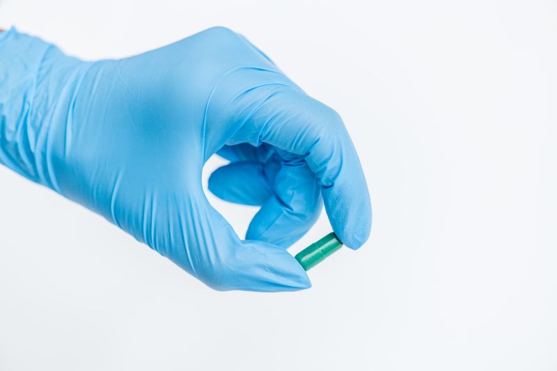 Closeup of gloved hand holding single drug capsule over white background, medicine and treatment concept